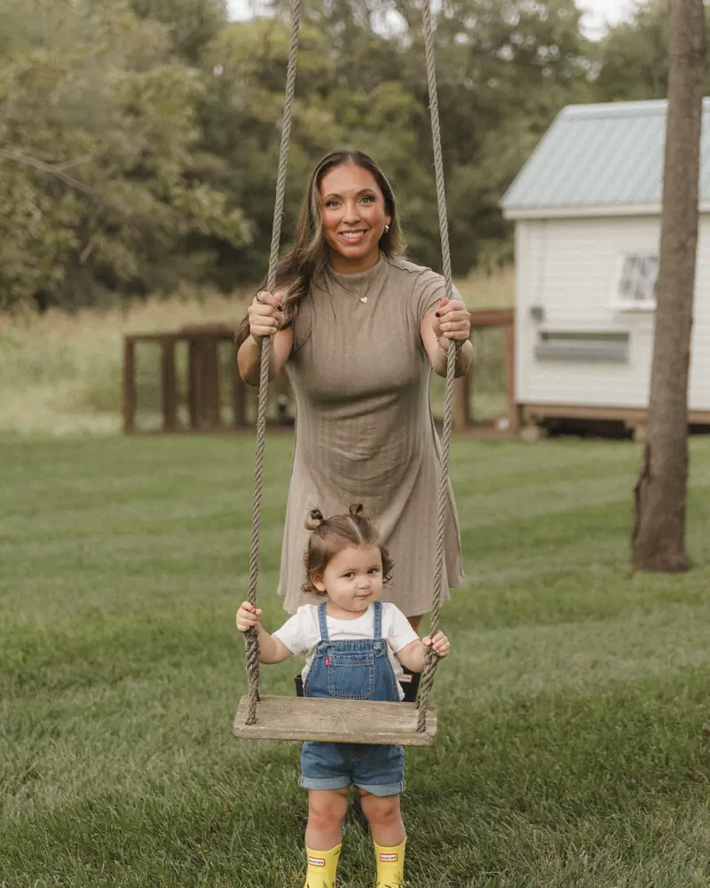 Alli pushing Summer on a rope swing in yellow rain boots